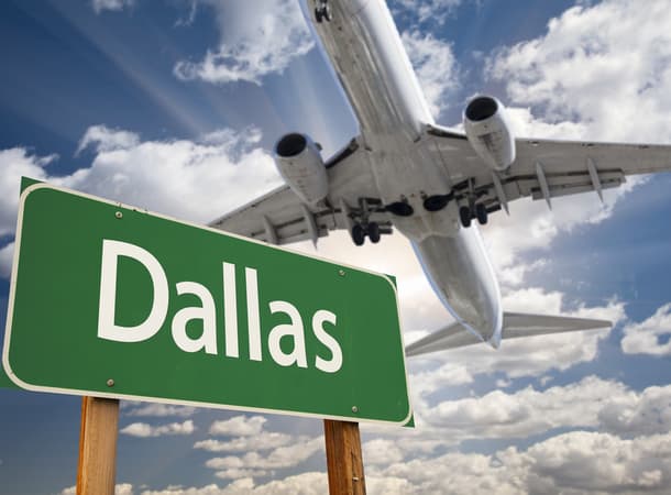 A plane flying over a green street sign reading "Dallas"